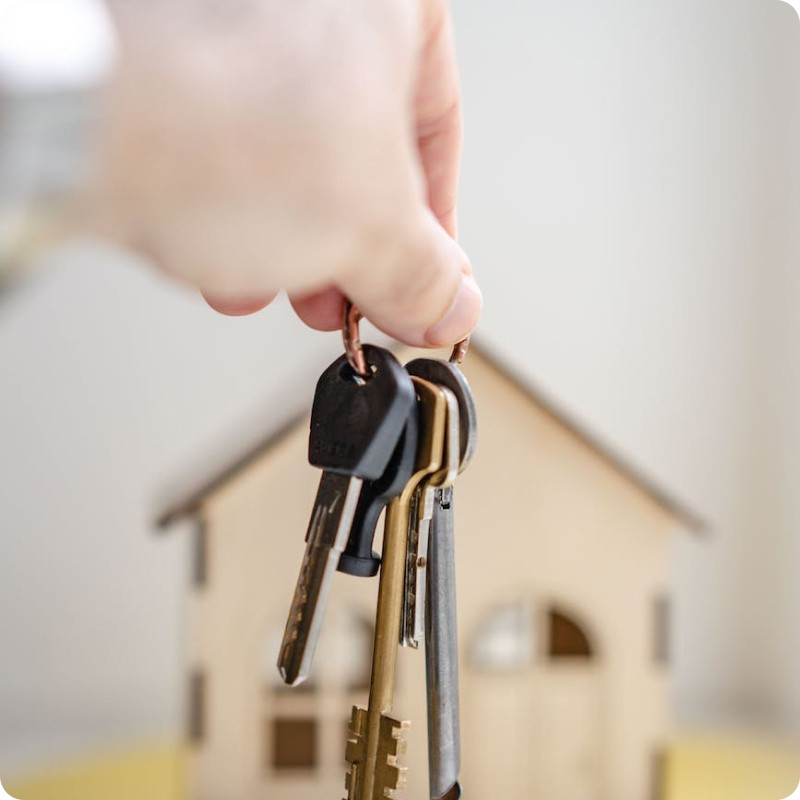 Person holding keys in front of mini house
